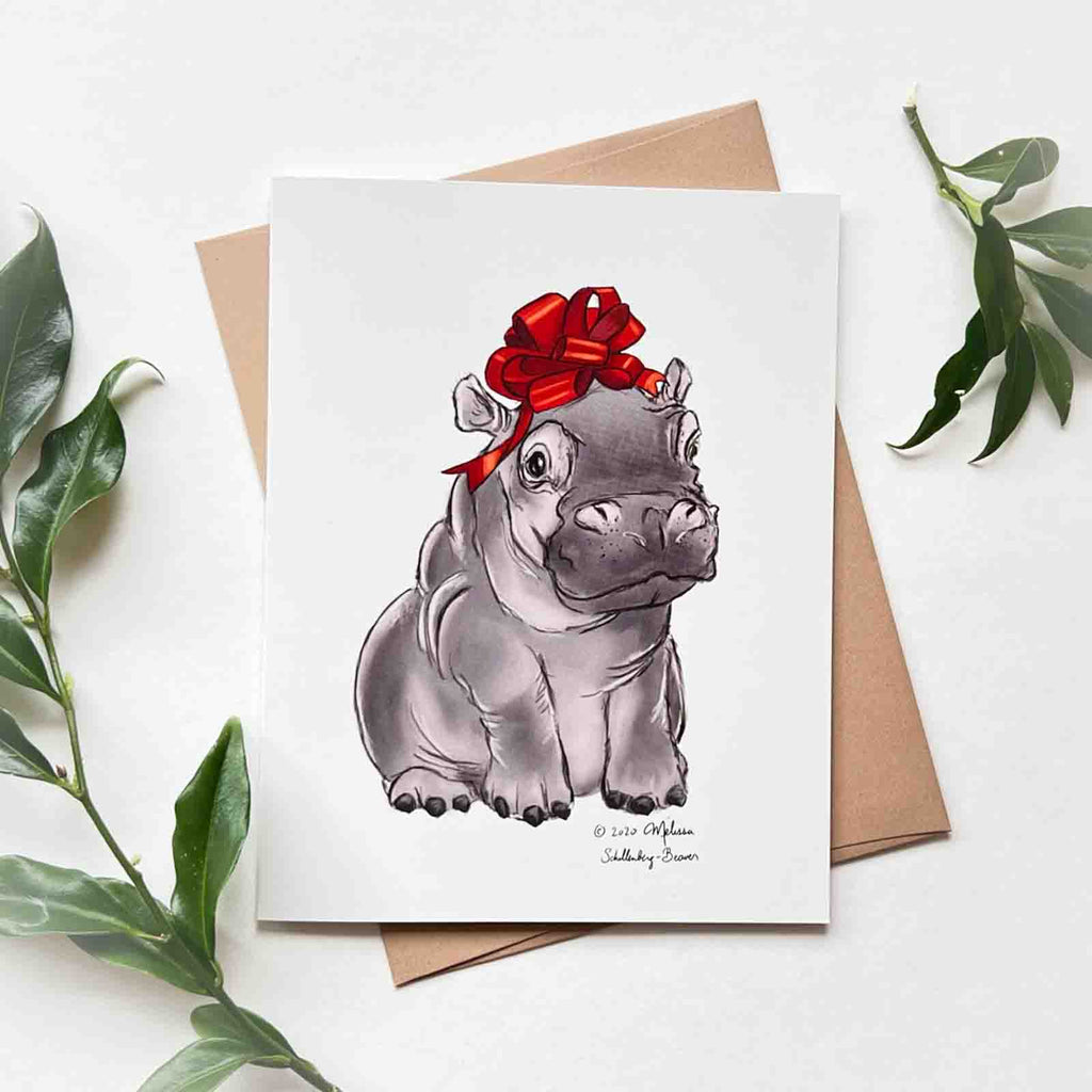 a baby hippopotamus with a red bow on its head